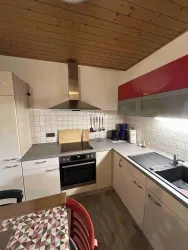 Eine moderne Küche mit Holzdecken und hellen Schränken. Sie enthält Kochutensilien, einen Herd und eine Spüle.