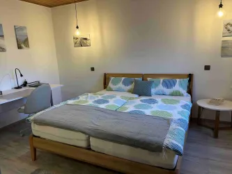 Ein modernes Schlafzimmer mit einem großen Bett und farbigen Bettdecken. Ein Schreibtisch und eine Lampe ergänzen die gemütliche Atmosphäre.