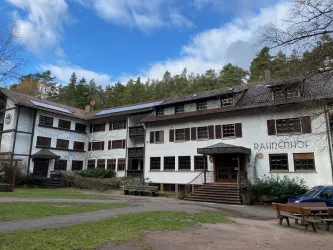 Ein historisches Gebäude mit weißen Wänden und braunen Fensterrahmen. Es liegt in einer natürlichen Umgebung mit Bäumen und grünem Gras.