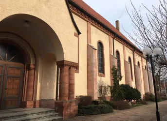 Ein beeindruckendes Gebäude mit einer traditionellen Fassade und großen Fenstern. Im Vordergrund befinden sich Grünpflanzen und Laternen.