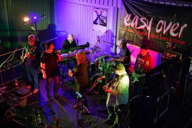 Eine Liveband spielt auf einer Bühne mit bunten Lichtern. Die Musiker scheinen viel Spaß zu haben und das Publikum zu begeistern.
