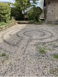 Ein Labyrinth aus Steinen in einem Garten. Umgeben von Grünpflanzen und einem ruhigen Ambiente.