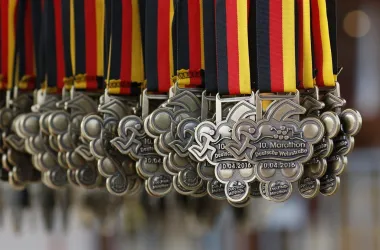 Eine Reihe von Medaillen hängt in einer Linie, jede mit einem bunten Band in Schwarz, Rot und Gold. Die Medaillen sind für den 10. Marathon der Deutschen Weinmeisterschaft.