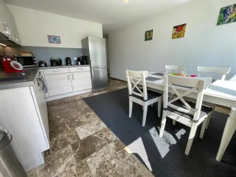 Eine moderne Küche mit einem weißen Essbereich und einem großen Fenster. Der Raum ist hell und aufgeräumt, mit verschiedenen Küchengeräten und einem stylischen Bodenbelag.