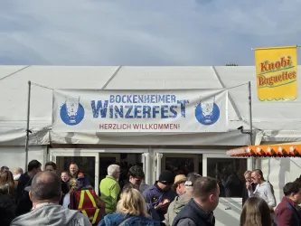Ein Zelt mit dem Banner "Bockenheimer Winzerfest" und dem Schriftzug "Herzlich Willkommen". Viele Menschen stehen davor und genießen die Atmosphäre.