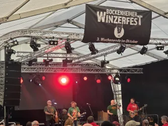 Eine Band spielt auf der Bühne eines Festzeltes beim Bockenheimer Winzerfest. Im Hintergrund hängt ein Banner, das auf das Event hinweist.