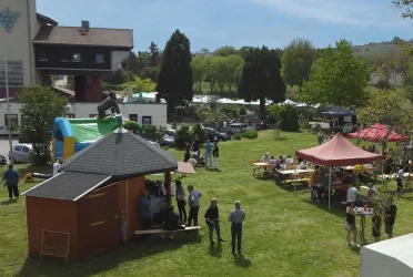 Eine Veranstaltung im Freien mit vielen Menschen auf einer Wiese. Es gibt Essensstände, eine Sprungburg und ein schönes Wetter.