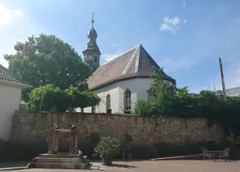 Eine charmante Kirche mit einem schlichten Turm und grünen Bäumen im Vordergrund. Der Himmel ist blau und die Stimmung friedlich.