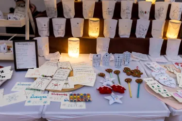Ein Tisch mit handgefertigten Artikeln, darunter Karten, Lichter und Deko-Objekte. Im Hintergrund steht eine Reihe beleuchteter Papierlaternen.