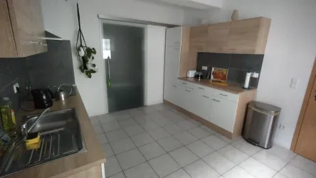 Eine moderne Küche mit hellen Holzmöbeln und grauen Wänden. Die Ausstattung umfasst ein Spülbecken, einen Kühlschrank und eine glasierte Tür.