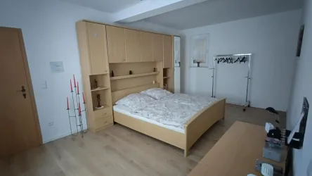 Ein helles Schlafzimmer mit einem Doppelbett und einem großen Kleiderschrank. Der Raum hat einen modernen, minimalistischen Stil und eine Holzfußboden.