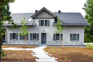 Ein modernes Haus mit grauen Fensterläden und einem schlichten Design. Der Garten ist gepflegt und enthält einige junge Bäume.