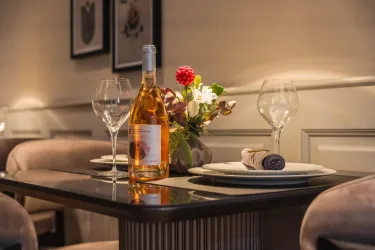 Ein elegant dekorierter Tisch mit einem Flasche Roséwein und zwei Gläsern. Ein Blumenarrangement und zwei Teller runden das gemütliche Ambiente ab.