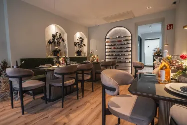 Ein elegantes Restaurant mit modernen Möbeln und einer gemütlichen Atmosphäre. Dekorative Pflanzen und Weinregale ergänzen das ansprechende Ambiente.