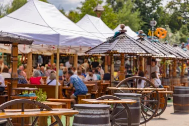 Ein lebhaftes Fest mit vielen Menschen, die unter weißen Zelten sitzen. Rustikale Tische und Stühle schaffen eine einladende Atmosphäre im Freien.