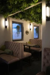 Ein gemütlicher Innenbereich mit gepolsterten Sitzbänken und einer grünen, pflanzenreichen Decke. Die Wände sind mit Fenstern und modernen Lampen ausgestattet.