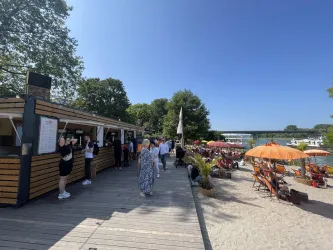 Ein belebtes Strandcafé mit Menschen und bunten Sonnenschirmen. Die Sonne scheint und es gibt viele Liegestühle zum Entspannen.