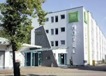 Ein modernes Hotelgebäude mit einer klaren Fassade und einem Eingangsbereich. Umgeben von Bäumen und unter blauem Himmel.