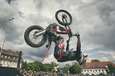 Ein Fahrer führt einen spektakulären BMX-Trick in der Luft aus. Die Zuschauer im Hintergrund beobachten gebannt das Geschehen.