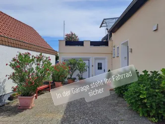 Ein gemütlicher Außenbereich mit wunderschönen Pflanzen. Im Hintergrund ist eine Garage zu sehen, die Platz für Fahrräder bietet.