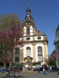 Eine beeindruckende Kirche mit einer markanten Architektur. Vor der Kirche blühen rosa Bäume und Menschen schlendern auf dem Platz.