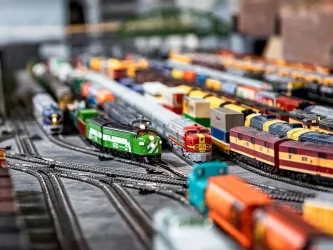 Eine Vielzahl von Modelleisenbahnen fährt auf einem detaillierten Gleisnetz. Die farbenfrohen Züge stehen dicht beieinander in einer lebhaften Modelllandschaft.