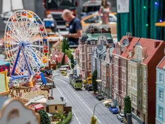 Eine detailreiche Modellstadt mit bunten Gebäuden und einem Riesenrad. Im Hintergrund sind Menschen zu sehen, die die Miniaturwelt betrachten.
