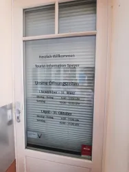 Eine Glastür mit einem Willkommensschild für die Tourist-Information in Speyer. Die Öffnungszeiten sind klar sichtbar auf dem Fenster aufgelistet.