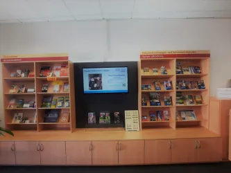 Ein Bücherregal mit verschiedenen Broschüren und Informationen. In der Mitte befindet sich ein Bildschirm, der zusätzliche Inhalte zeigt.
