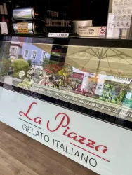 Ein Schaufenster mit einer großen Auswahl an italienischem Gelato. Darüber steht der Name "La Piazza" in auffälliger Schrift.