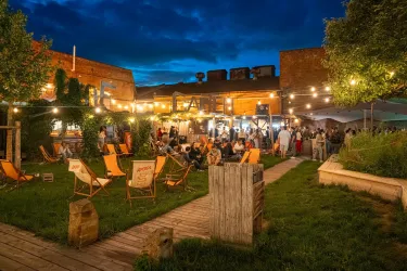 Eine gemütliche Außenfläche mit vielen Menschen, die sich treffen und entspannen. Die Szene ist mit Lichtern geschmückt und bietet eine einladende Atmosphäre.