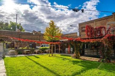 Ein gemütlicher Außenbereich mit grüner Wiese und Holzwegen. Im Hintergrund sind Gebäude und dekorative Pflanzen zu sehen.