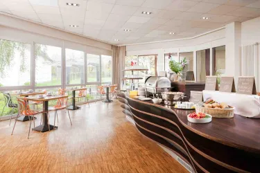 Ein einladender Frühstücksraum mit großen Fenstern und modernem Mobiliar. Der Buffetbereich bietet eine Auswahl an Speisen und Getränken.