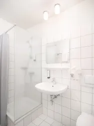 Ein modernes Badezimmer mit einer Dusche und einem Waschbecken. Die Wände sind gefliest und die Beleuchtung ist hell.