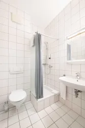 Ein modernes Badezimmer mit hellen Fliesen. Es enthält eine Dusche, ein Waschbecken und eine Toilette.