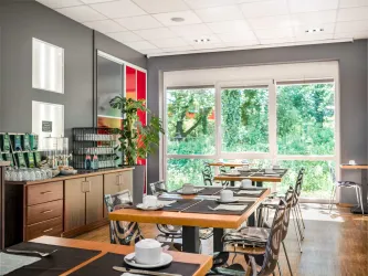 Ein modernes Restaurant mit hellen, freundlichen Farben und großen Fenstern. Die Tische sind elegant eingedeckt und die Umgebung bietet einen Blick ins Grüne.
