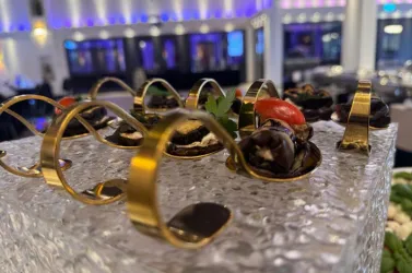 Ein elegantes Gericht mit Muscheln und einer Tomate, präsentiert auf einer gläsernen Platte. Das dekorative Design umfasst goldene Elemente und frische Kräuter.