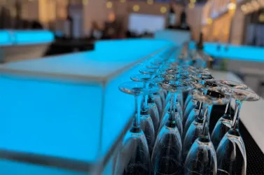 Eine stilvolle Bar mit leuchtend blauen Lichtern. Gläser sind ordentlich aufgereiht und warten auf die Gäste.