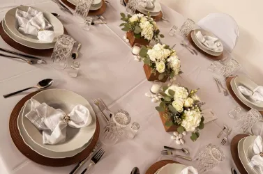 Ein elegant gedeckter Tisch mit weißen Blumenarrangements und dekorativem Geschirr. Die Atmosphäre ist festlich und einladend.
