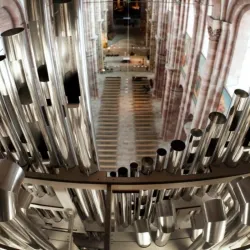 Eine beeindruckende Orgel mit vielen metallischen Pfeifen ist im Vordergrund zu sehen. Im Hintergrund erstreckt sich der große Raum einer Kirche.