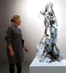Eine Frau betrachtet eine filigrane Skulptur aus Papier. Die Skulptur hat eine komplexe Form und schimmert in Weiß und Schwarz.