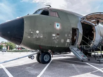 Ein militärisches Flugzeug steht auf einem Parkplatz. Der vordere Teil des Flugzeugs ist geöffnet, und eine Treppe führt hinein.