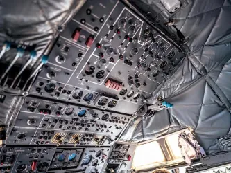 Ein Blick auf das Cockpit mit zahlreichen Steuerknöpfen und Instrumenten. Die Wände sind mit einer isolierenden Materialschicht bedeckt.