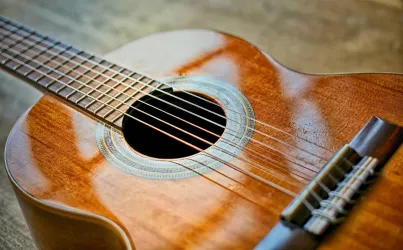 Eine akustische Gitarre mit einem glänzenden Holzfinish. Die Saiten sind sichtbar und der Klangkörper hat eine schöne runde Form.