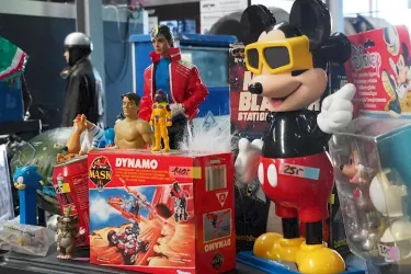Eine Sammlung von Vintage-Spielzeugen auf einem Tisch. Darunter sind Figuren von Mickey Mouse, He-Man und anderen Charakteren in verschiedenen Farben und Größen.