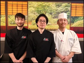 Drei Köche in schwarzen und weißen Uniformen stehen nebeneinander. Im Hintergrund ist eine traditionelle japanische Landschaft zu sehen.