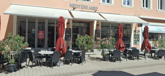 Ein mediterranes Restaurant mit Außenbereich. Rote Sonnenschirme und Tische laden zum Verweilen ein.