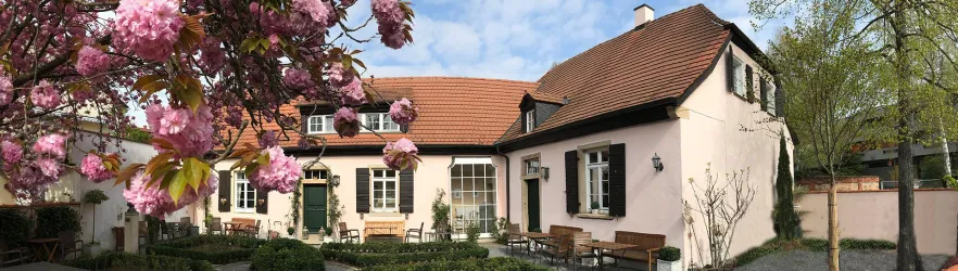 Ein hübsches Haus mit einem roten Dach und großen Fenstern. Im Vordergrund blühen rosa Blumen und es gibt eine ruhige Terrasse.