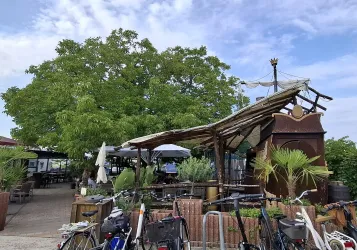 Ein gemütliches Restaurant mit viel Grün und einer liebevollen Einrichtung. Im Vordergrund stehen Fahrräder und Sonnenschirme laden zum Verweilen ein.