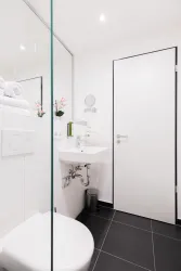 Ein modernes Badezimmer mit einer weißen Toilette und einem Waschbecken. Der Raum ist hell und minimalistisch eingerichtet, mit einer großen Spiegelfläche und Pflanzen.